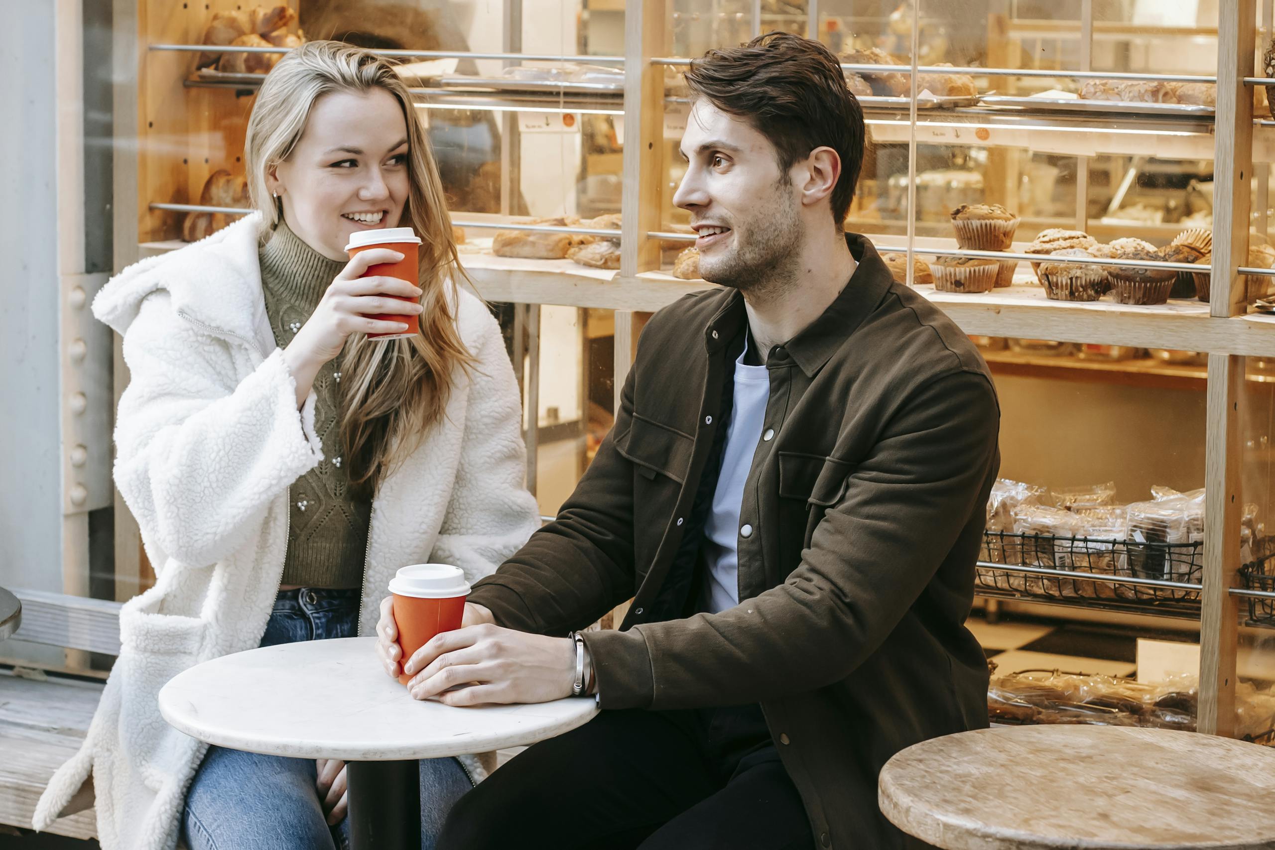 Young couple enjoying coffee outdoors near a bakery, capturing a moment of joy and connection.