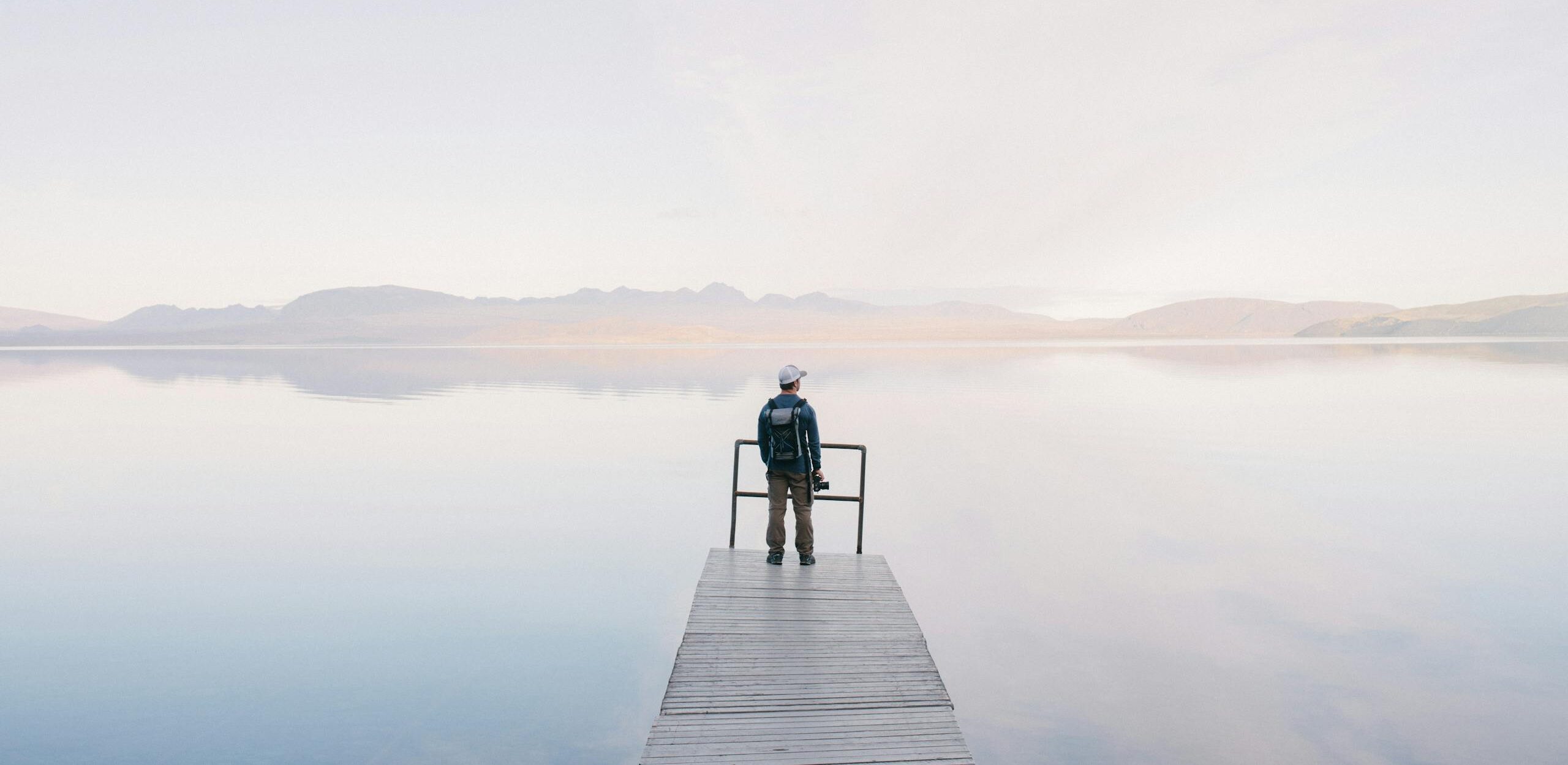 A solitary traveler stands on a dock enjoying the serene water view